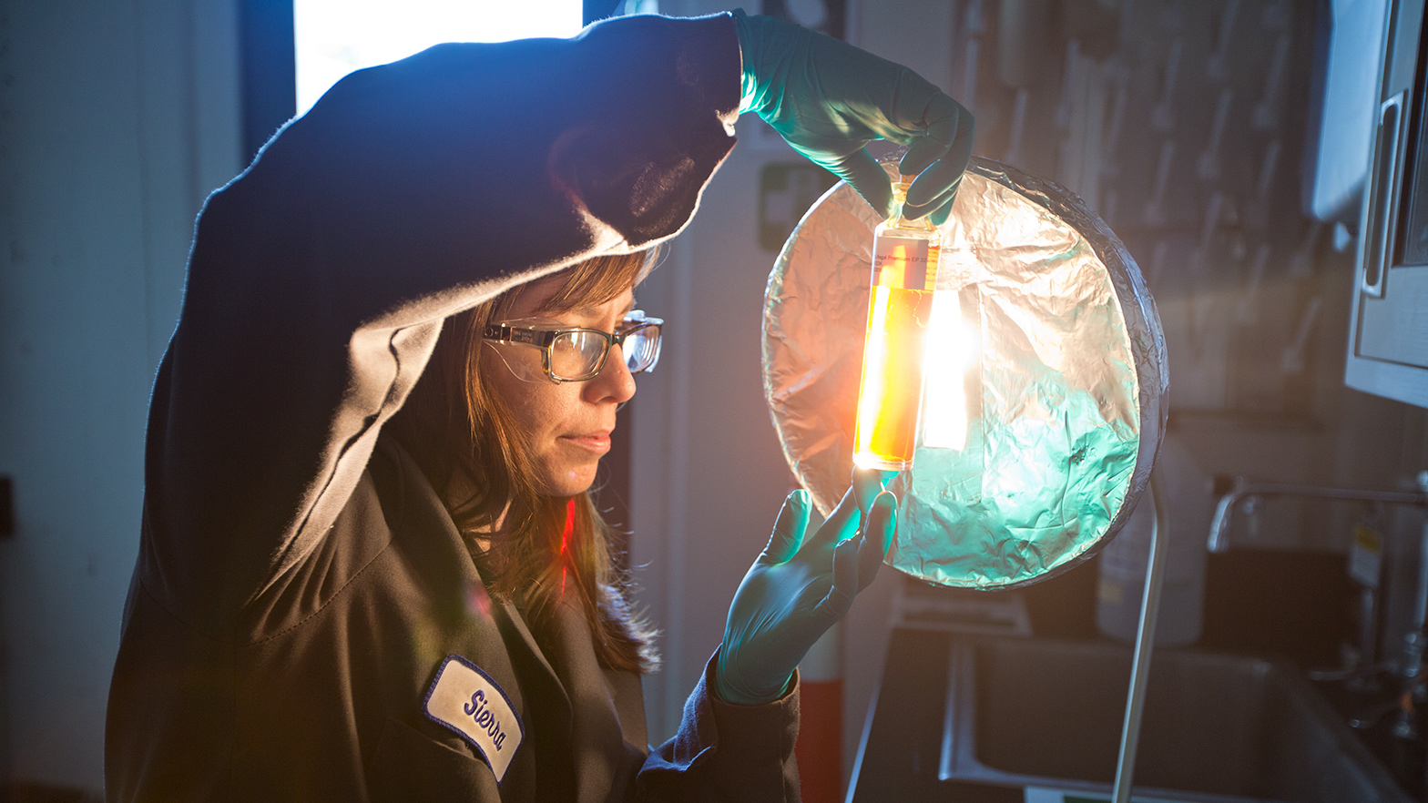 Worker looking at lubricant samples in front of lamp in the blend services laboratory at Richmond Technology Center, Richmond Refinery, California.